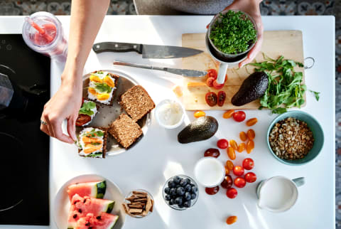 Overhead of woman cooking and preparing healthy meal with fresh avocado, veggies, watermelon, blueberries, and other fruit in kitchen